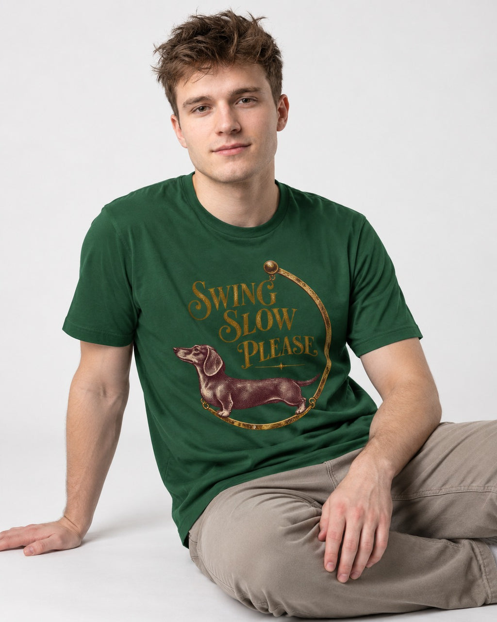 Dachshund Swing Slow Please Necklace Frame Graphic T-Shirt in Forest Green, worn by a seated model