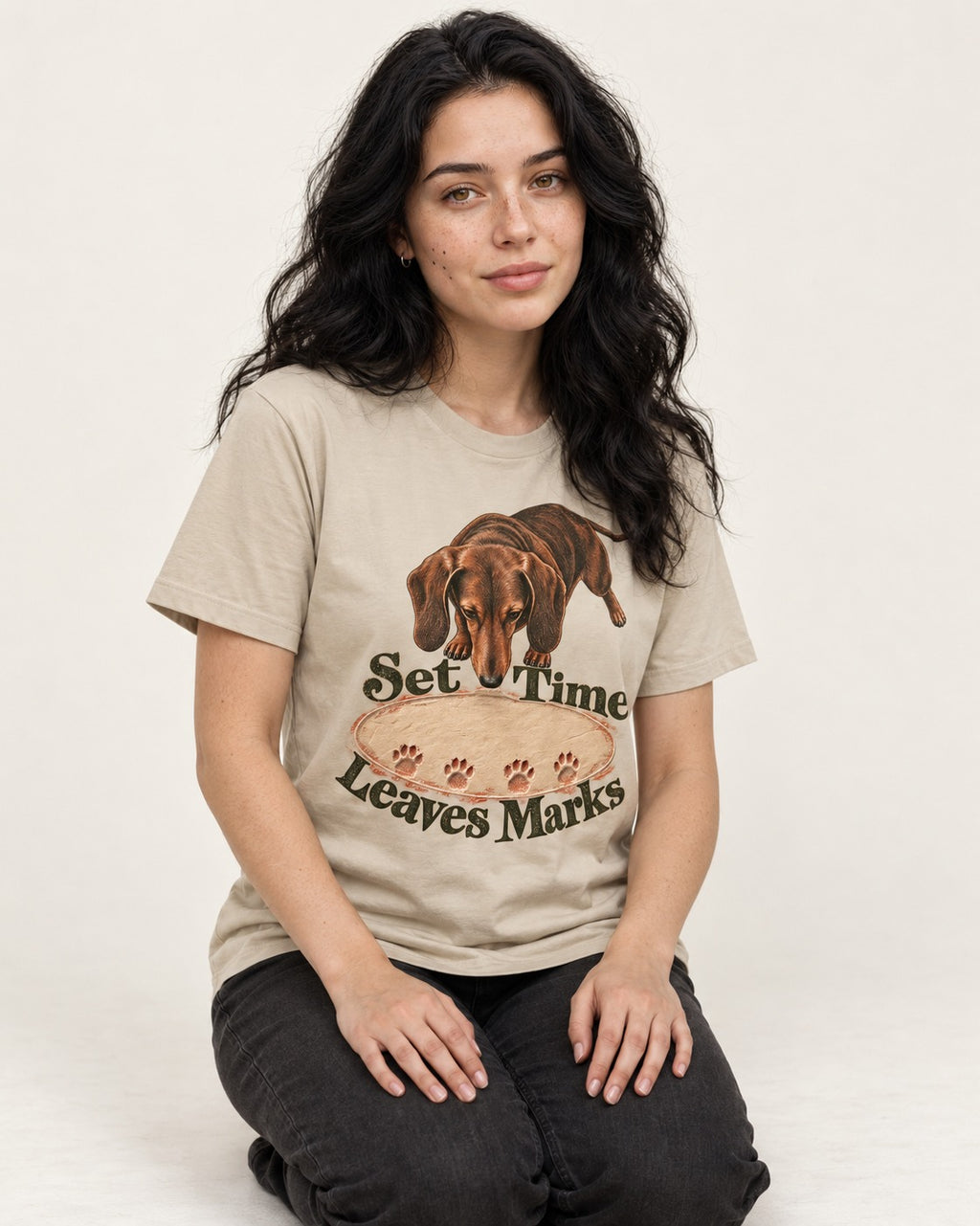 Dachshund Time Leaves Marks T-Shirt in Sand, worn by a seated model