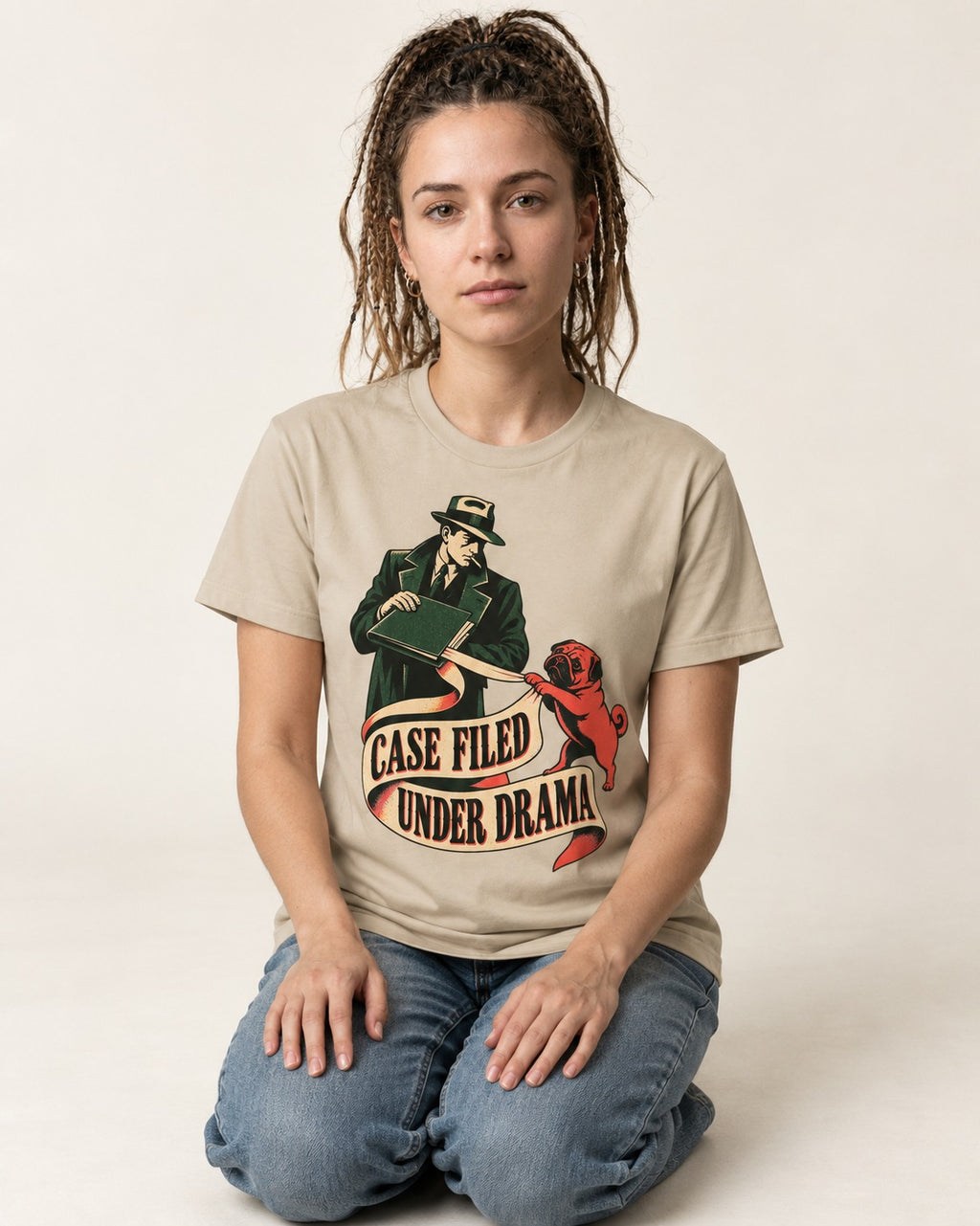 Pug Case Filed Under Drama T-Shirt in Sand, worn by a seated model