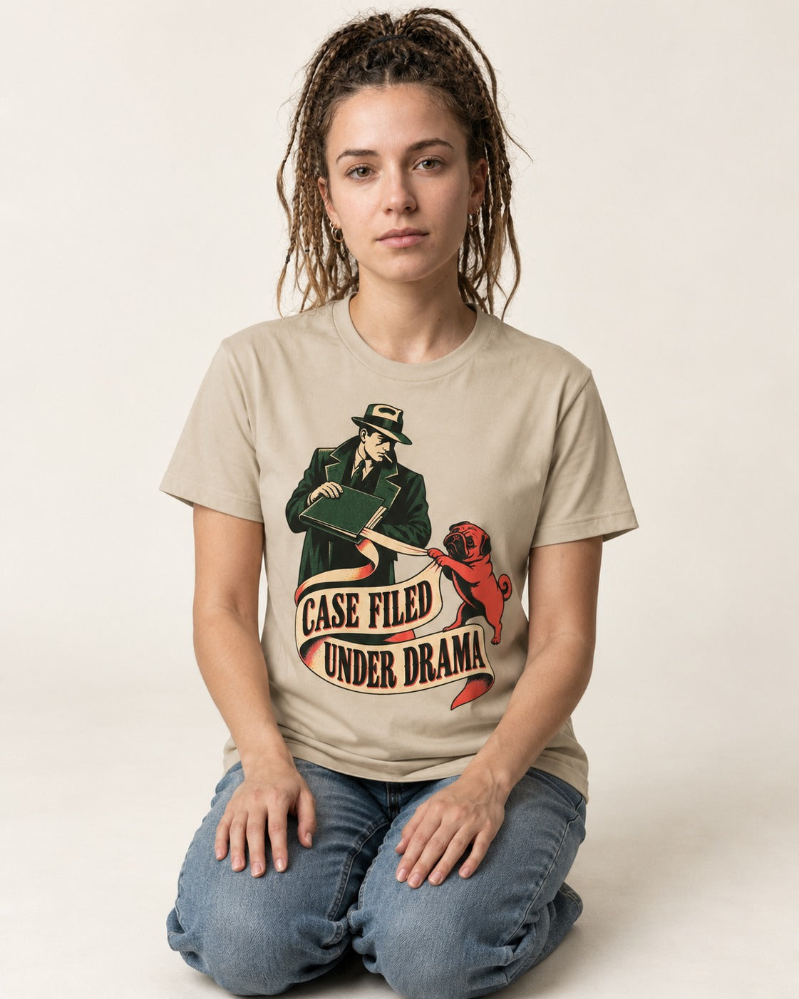 Pug Case Filed Under Drama T-Shirt in Sand, worn by a seated model