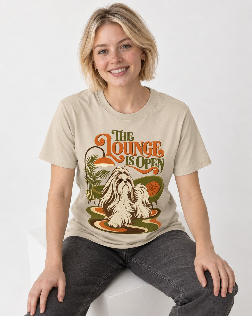 The Shih Tzu Lounge Is Open T-Shirt in Sand, worn by a seated model
