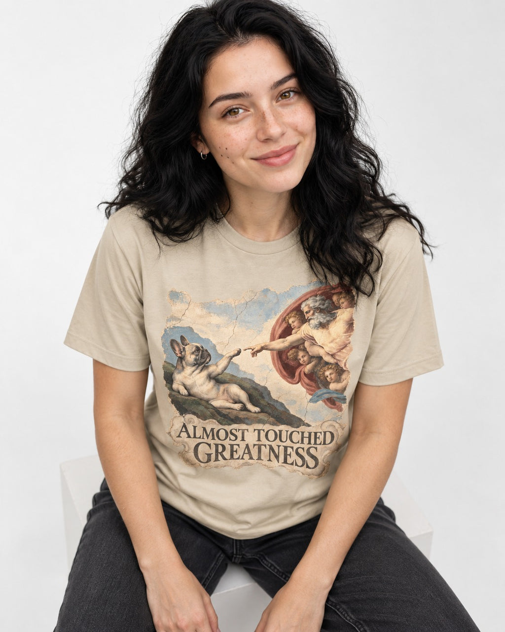 Frenchie Almost Touched Greatness T-Shirt in Sand, worn by a seated model