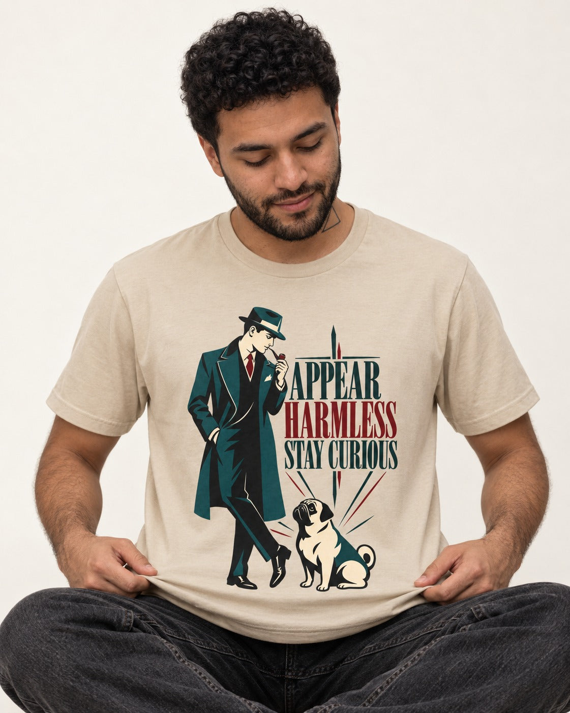 Pug Appear Harmless Stay Curious T-Shirt in Sand, worn by a seated model