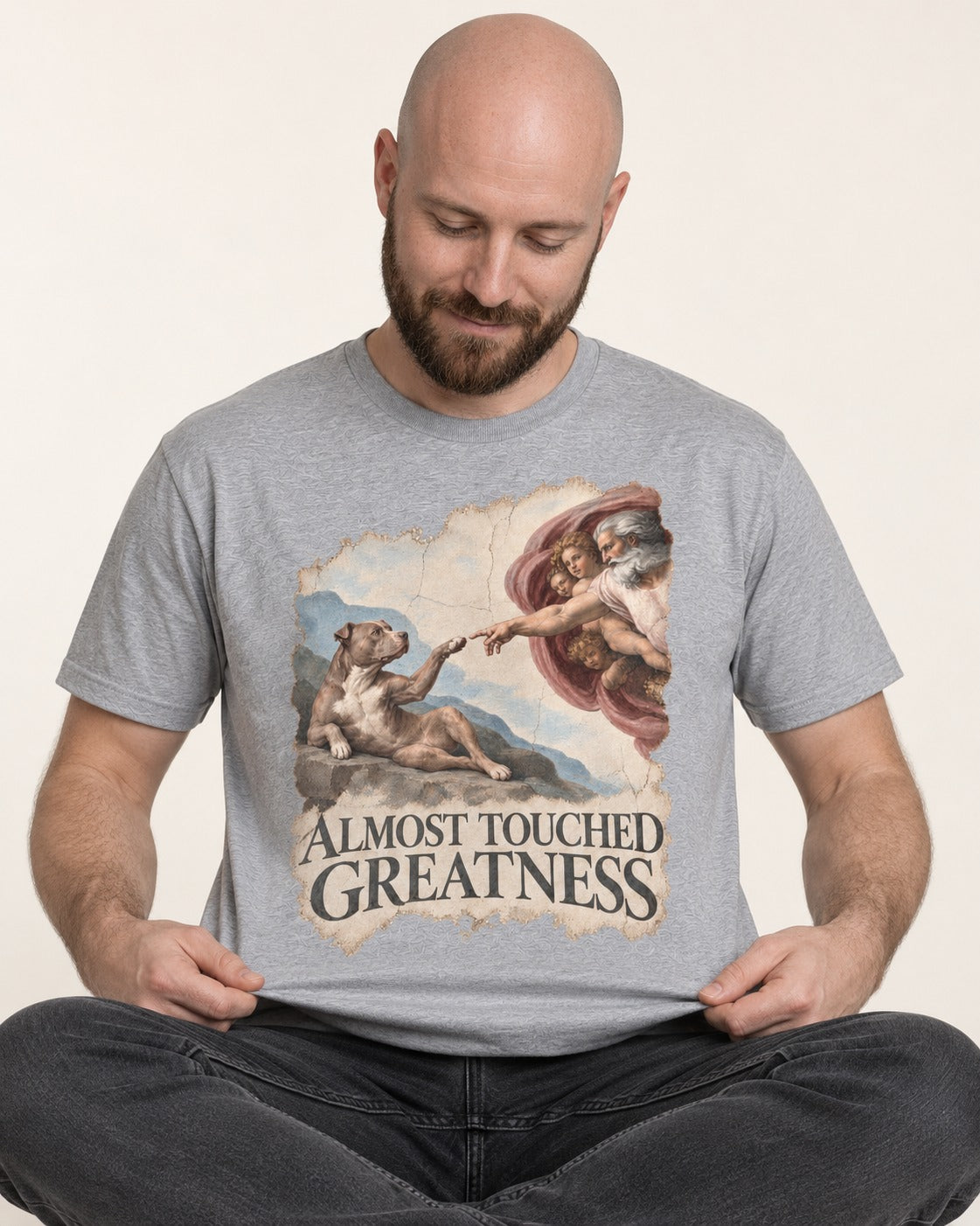 Pitbull Almost Touched Greatness Creation Parody Graphic T-Shirt in Sport Grey, worn by a seated model