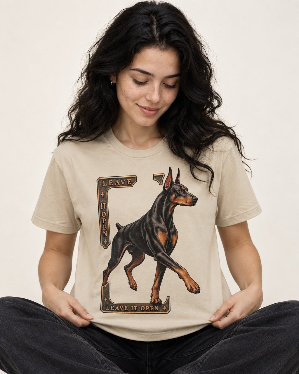 Leave It Open Doberman T-Shirt in Sand, worn by a seated model