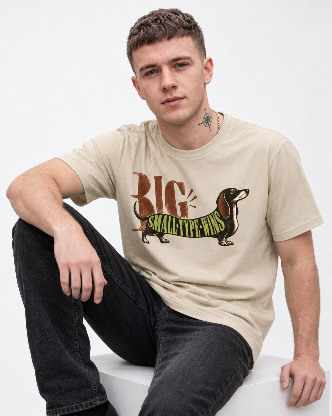 Dachshund Small Type Wins T-Shirt in Sand, worn by a seated model