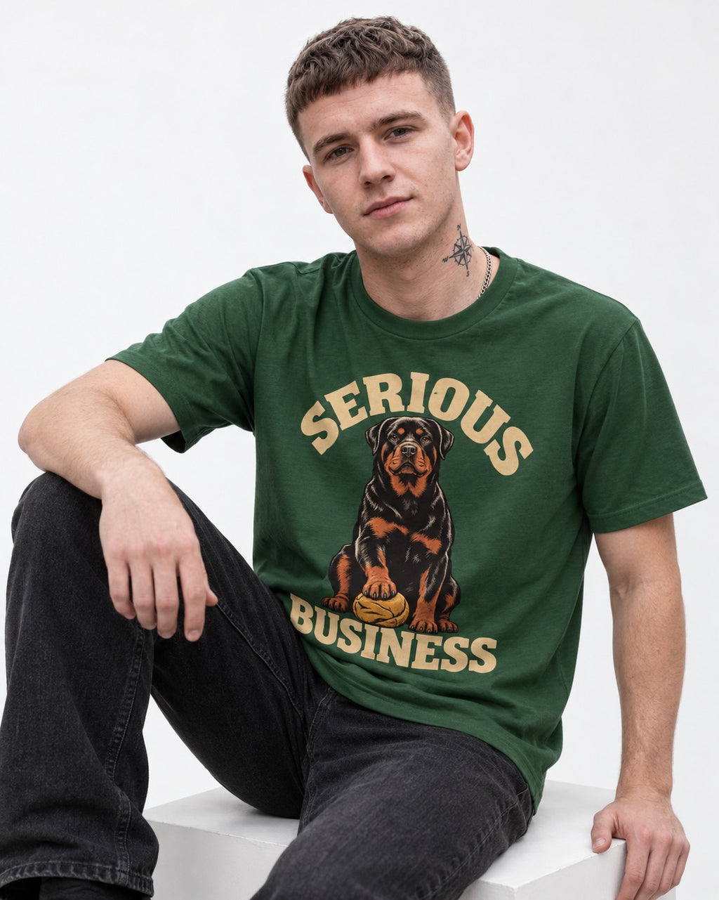 Rottweiler Serious Business Ball Under Paw Graphic T-Shirt in Forest Green, worn by a seated model