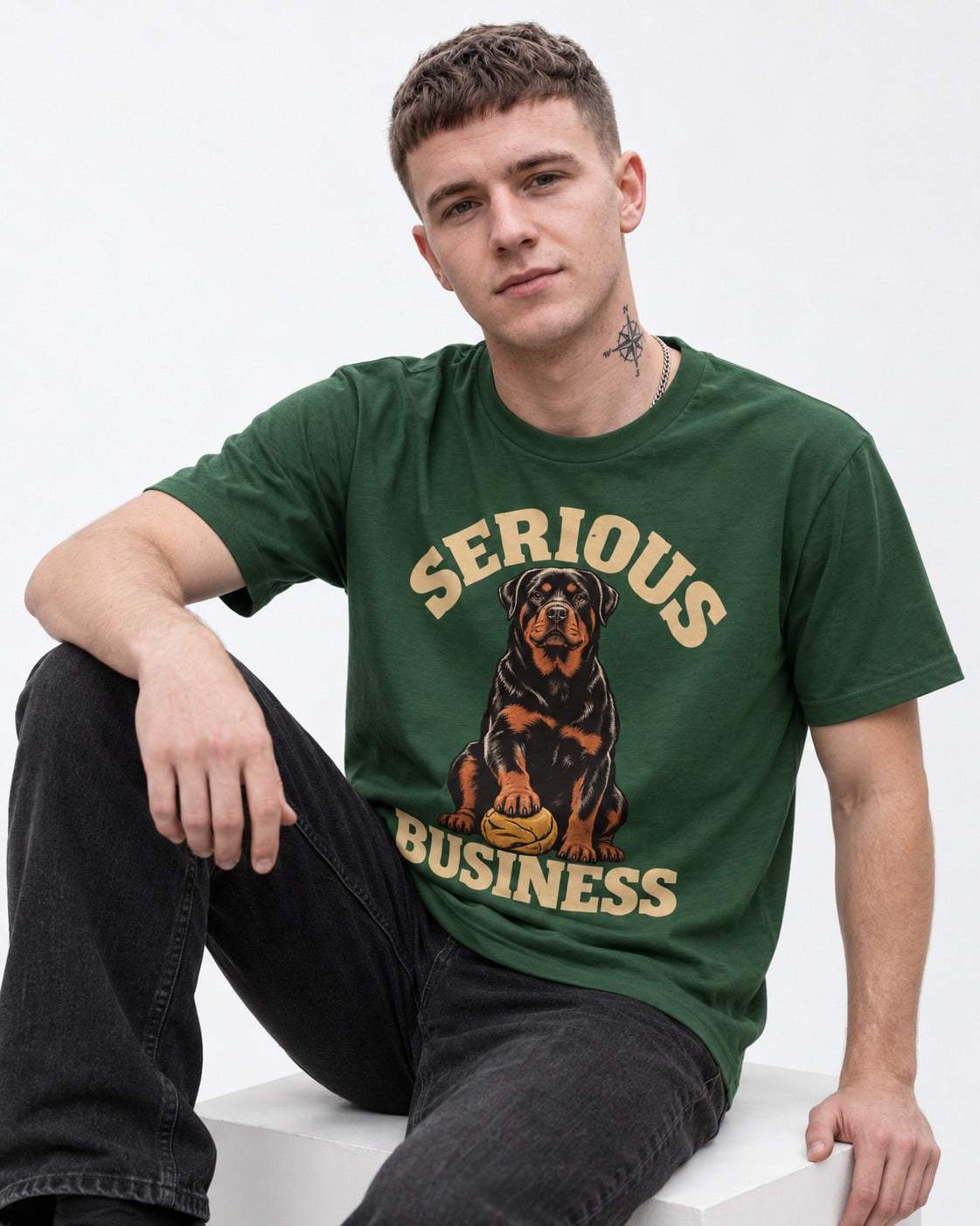 Rottweiler Serious Business Ball Under Paw Graphic T-Shirt in Forest Green, worn by a seated model