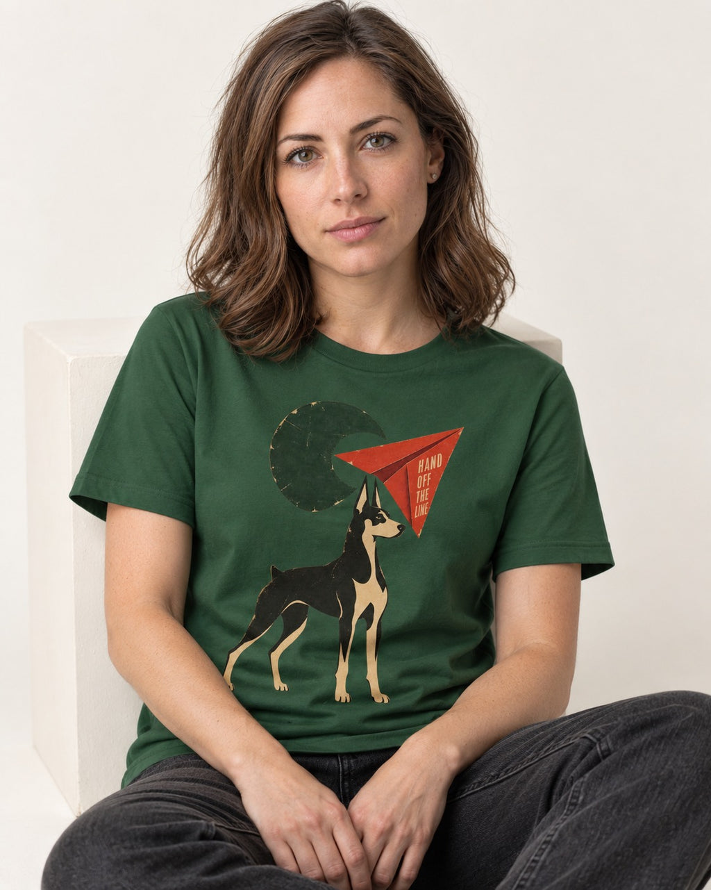 Doberman Hand Off the Line Paper Plane Graphic T-Shirt in Forest Green, worn by a seated model