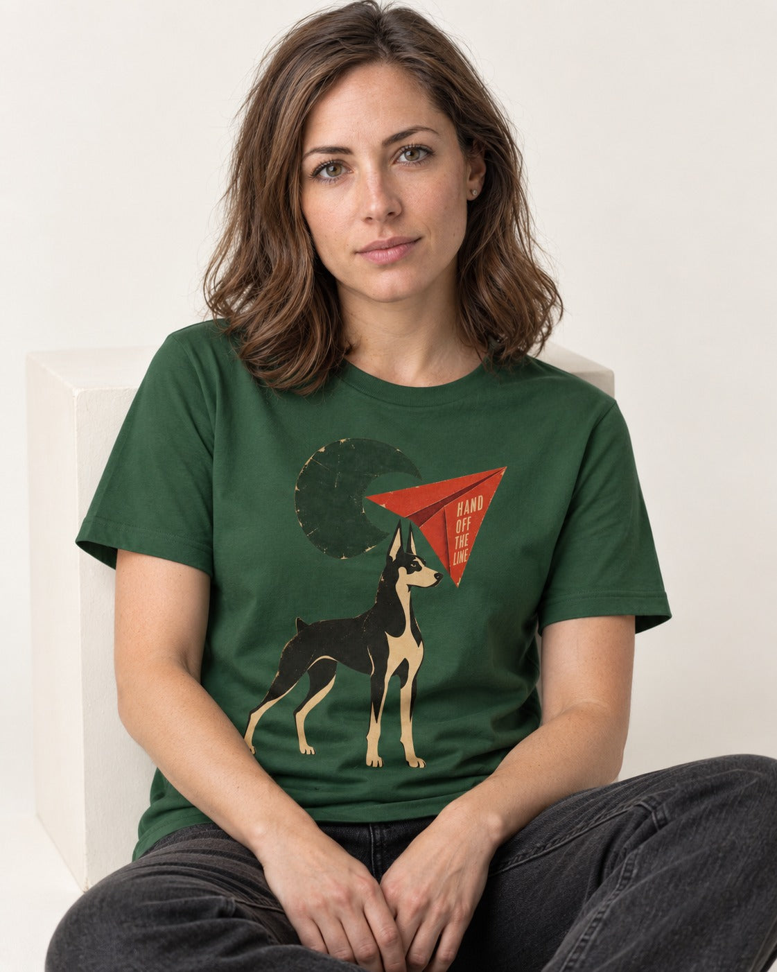 Doberman Hand Off the Line Paper Plane Graphic T-Shirt in Forest Green, worn by a seated model