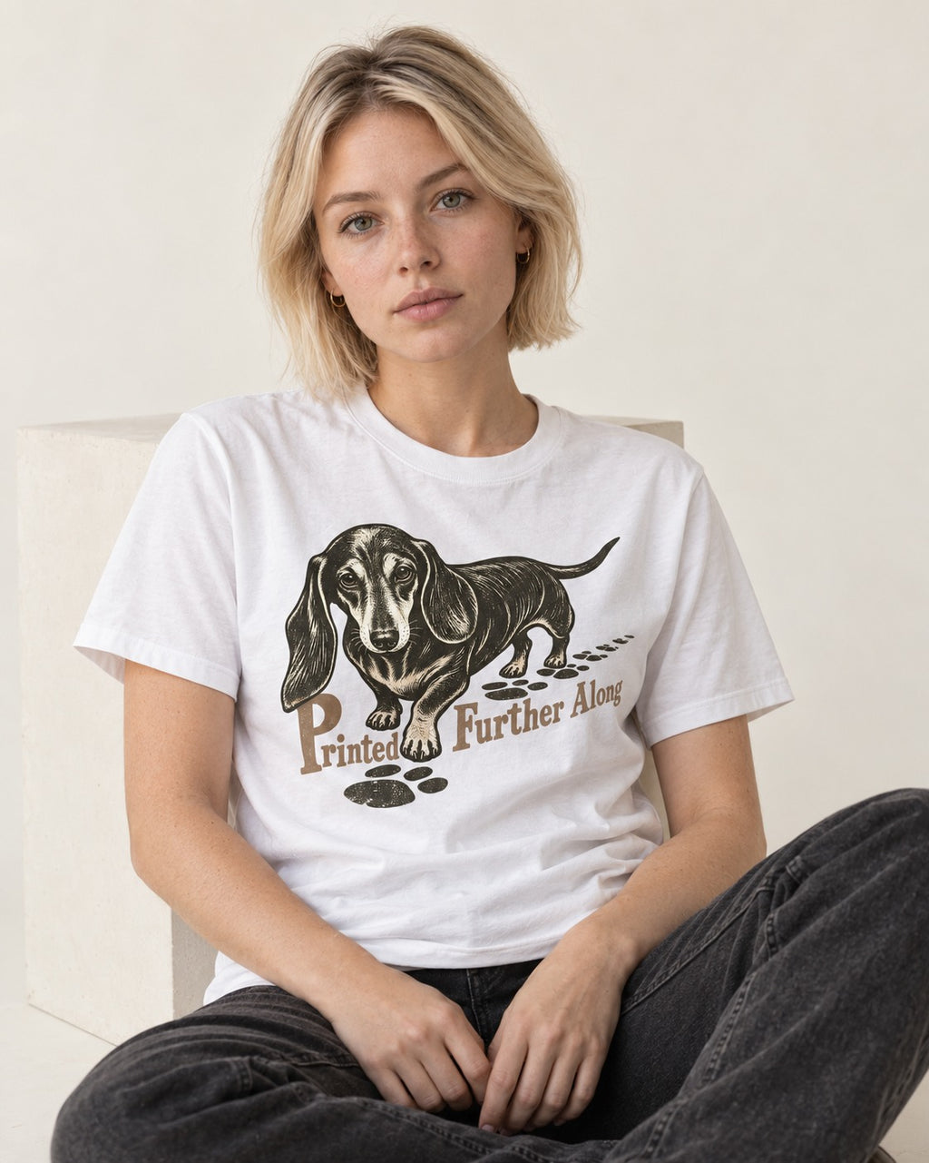 Dachshund Printed Further Along Footprint Graphic T-Shirt in White, worn by a seated model