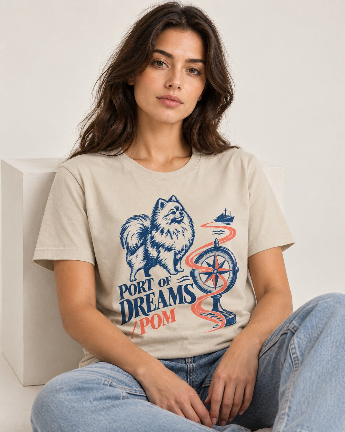 Pomeranian Port of Dreams T-Shirt in Sand, worn by a seated model