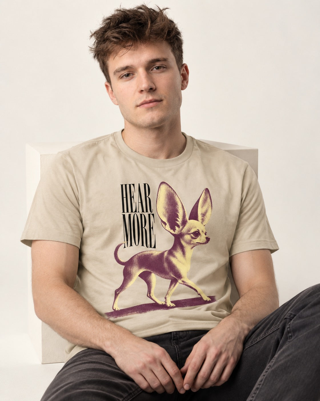 Hear More Chihuahua T-Shirt in Sand, worn by a seated model