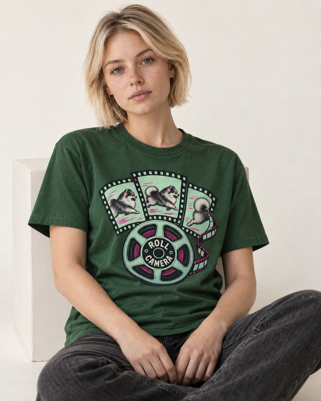 Pomeranian Roll Camera Film Reel Graphic T-Shirt in Forest Green, worn by a seated model