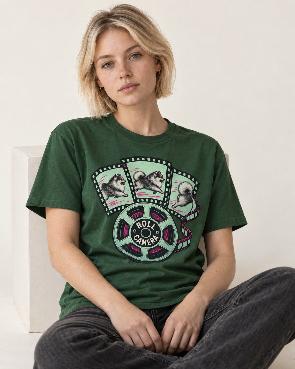 Pomeranian Roll Camera Film Reel Graphic T-Shirt in Forest Green, worn by a seated model