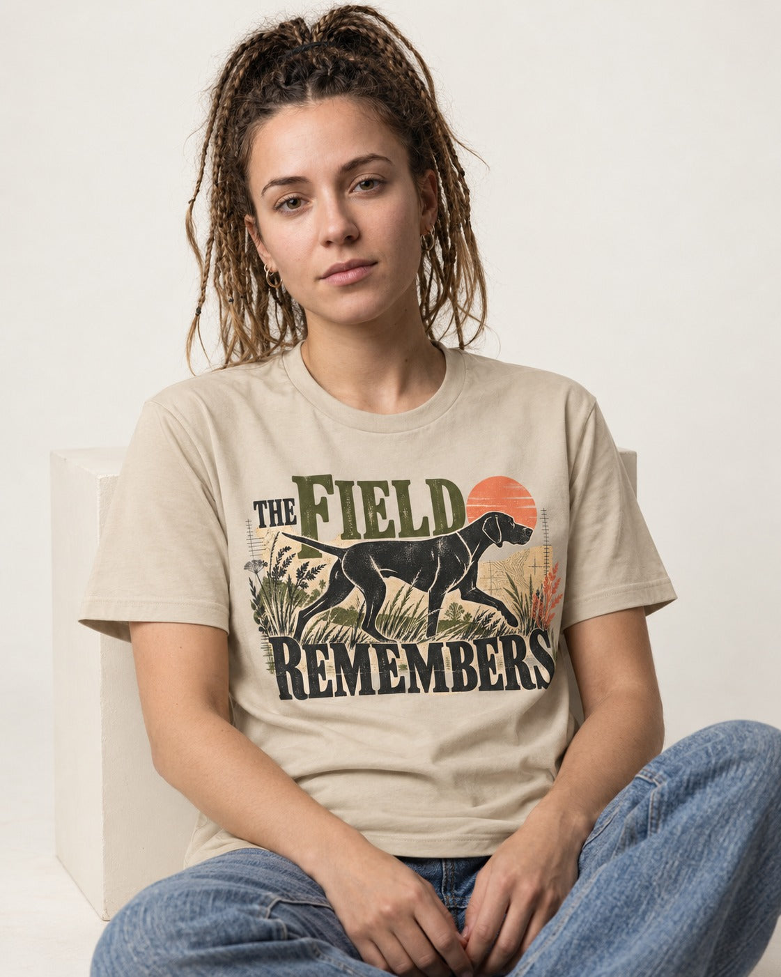 The Field Remembers German Shorthaired Pointer T-Shirt in Sand, worn by a seated model