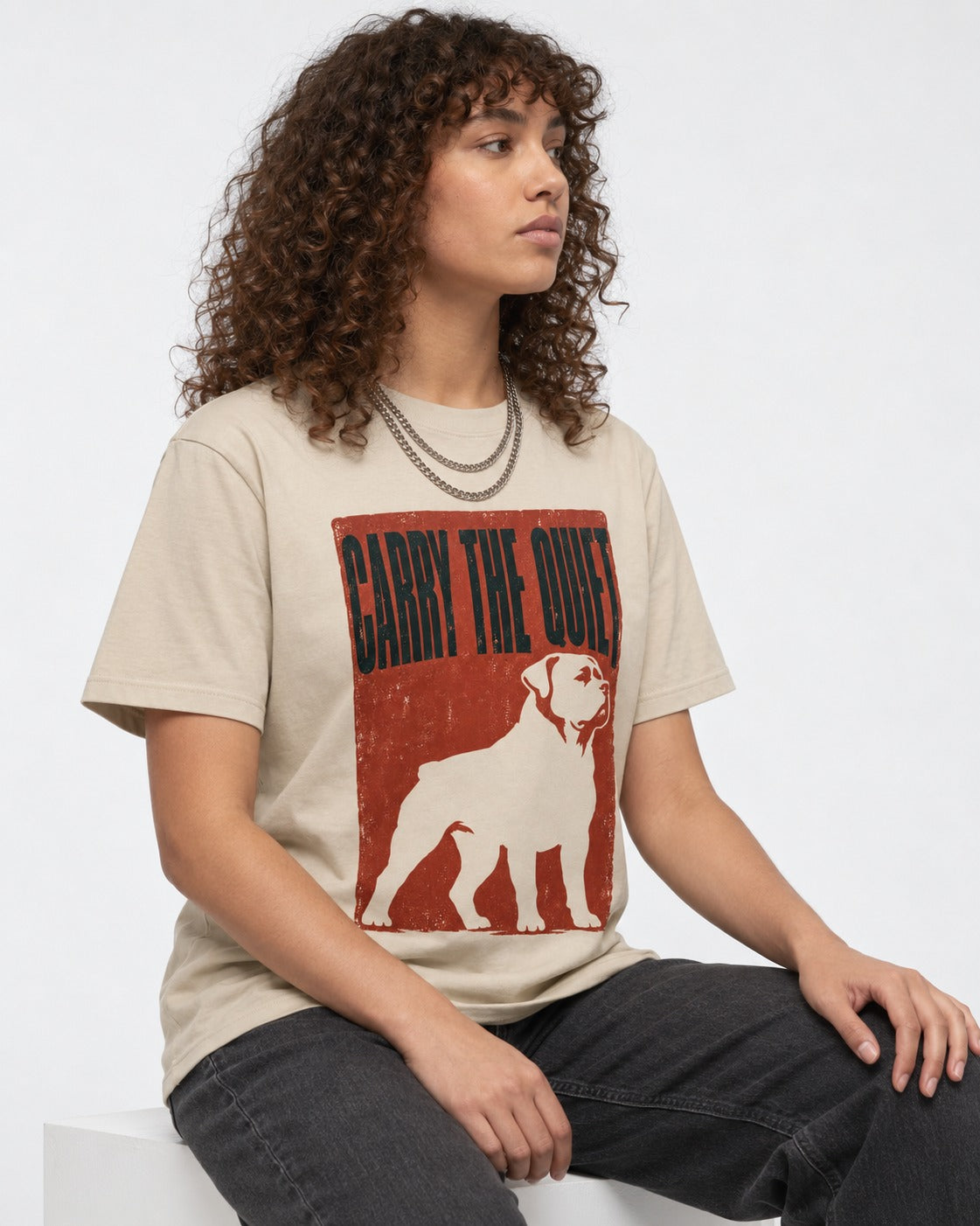Rottweiler Carry the Quiet T-Shirt in Sand, worn by a seated model