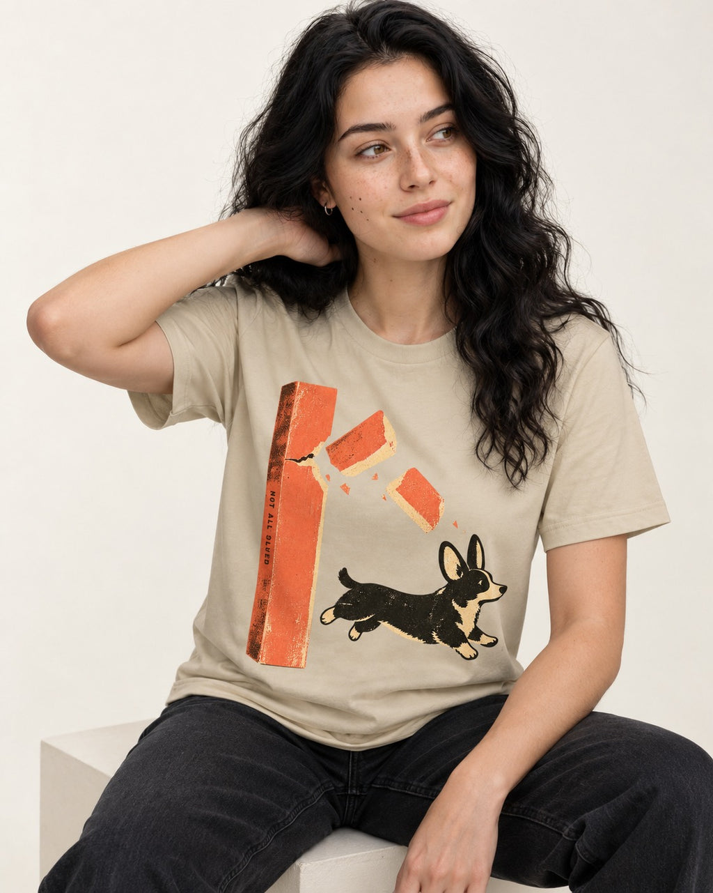 Not All Glued Corgi T-Shirt in Sand, worn by a seated model