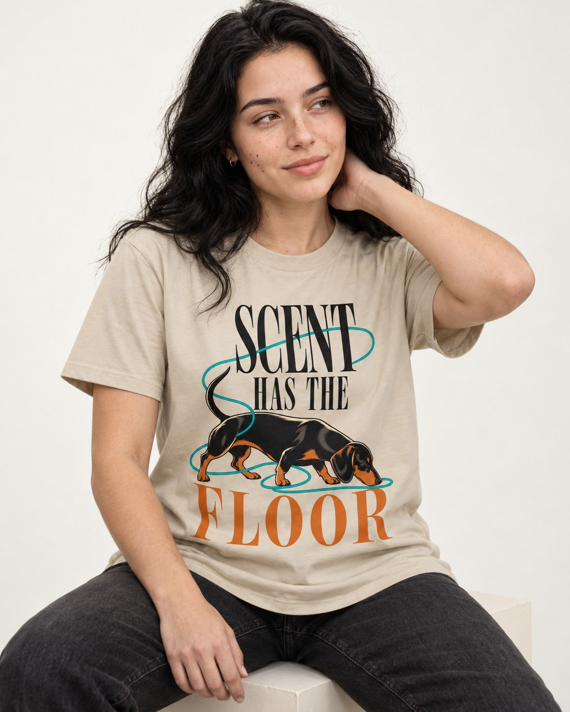 Dachshund Scent Has the Floor T-Shirt in Sand, worn by a seated model