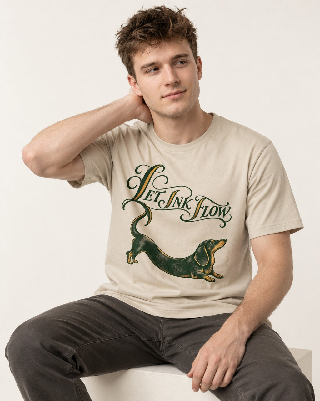 Let the Dachshund Ink Flow T-Shirt in Sand, worn by a seated model