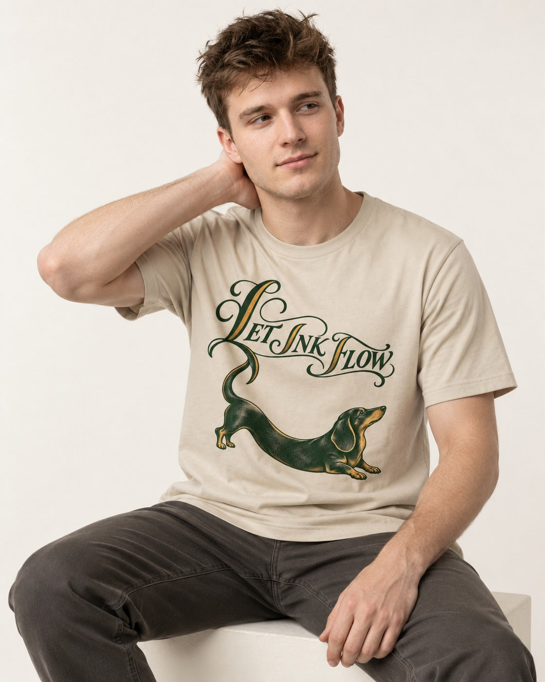 Let the Dachshund Ink Flow T-Shirt in Sand, worn by a seated model