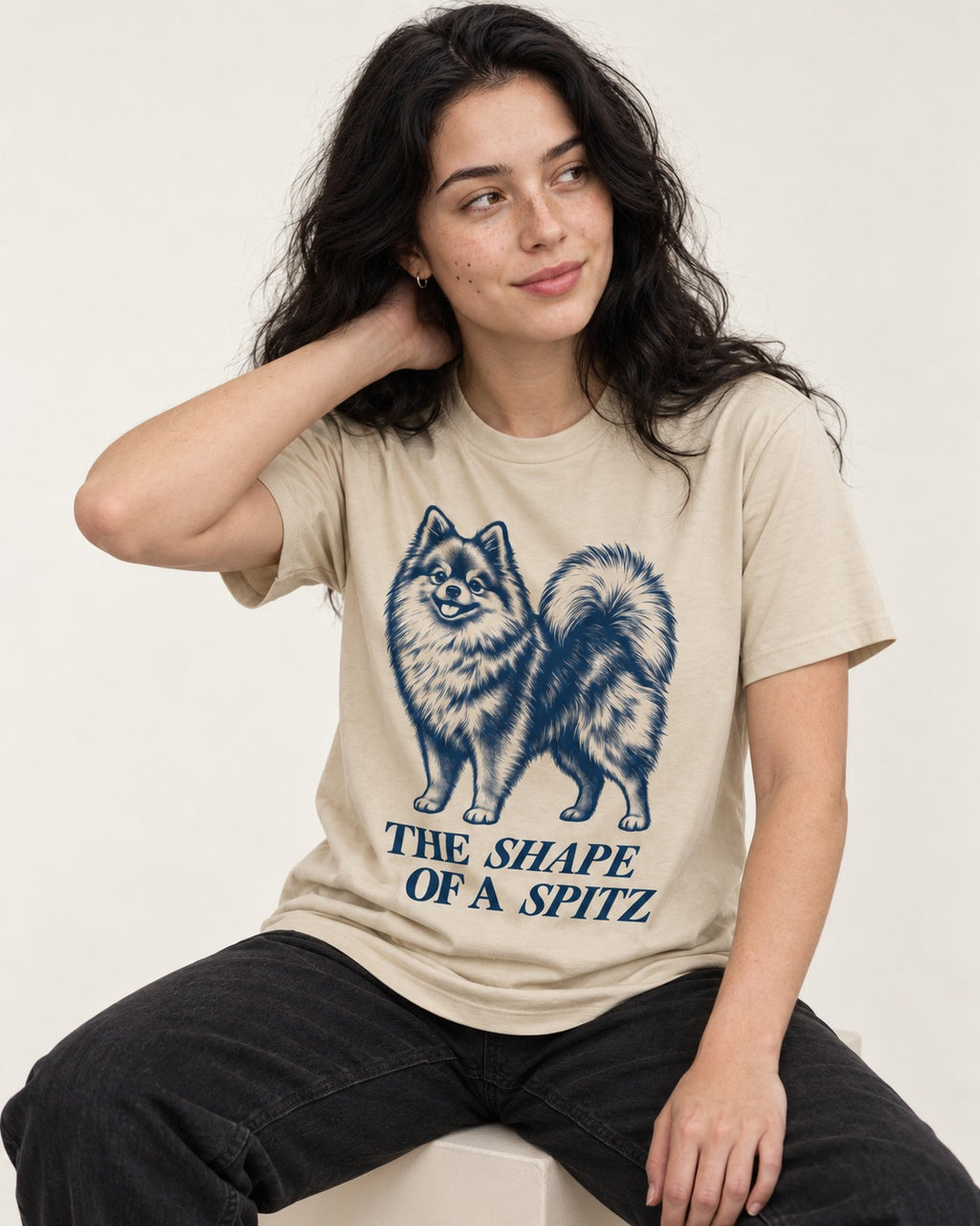 The Shape of a Pomeranian T-Shirt in Sand, worn by a seated model
