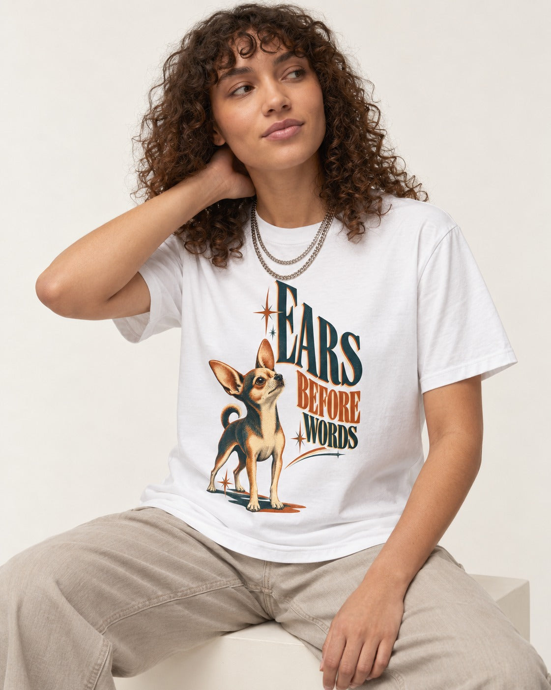 Chihuahua Ears Before Words Retro Typography T-Shirt in White, worn by a seated model