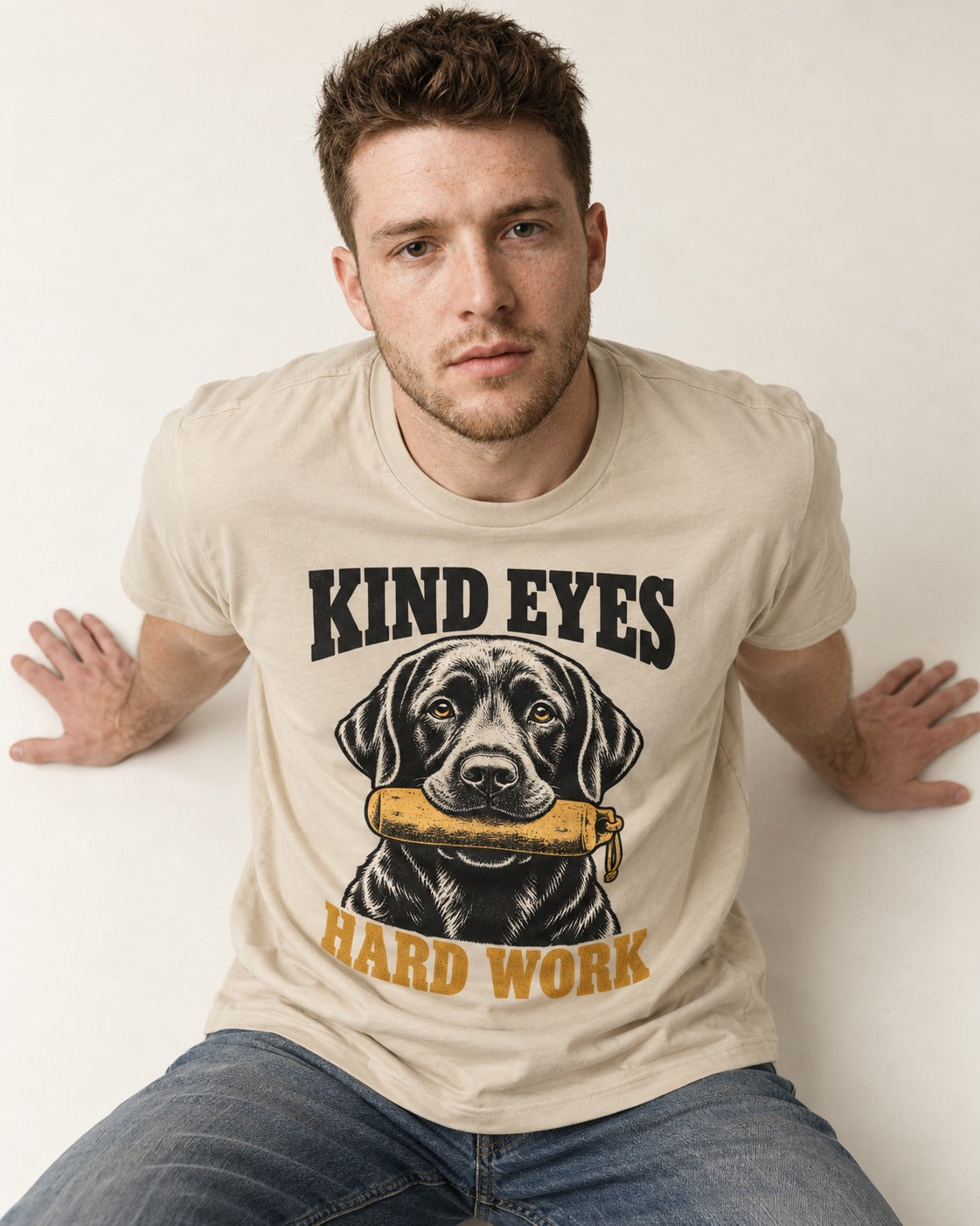 Kind Eyes Hard Work Labrador Retriever T-Shirt in Sand, worn by a seated model