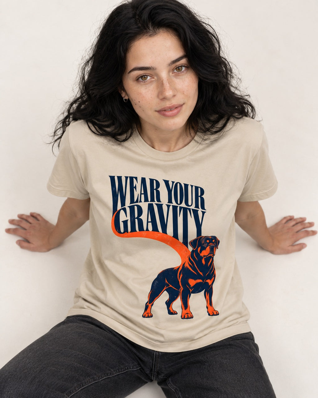 Wear Your Gravity Rottweiler T-Shirt in Sand, worn by a seated model