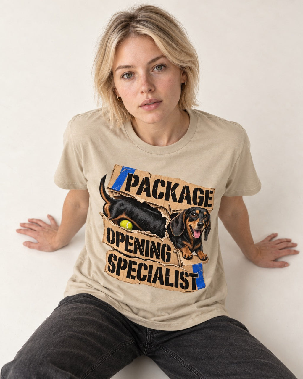 Dachshund Package Opening Specialist T-Shirt in Sand, worn by a seated model