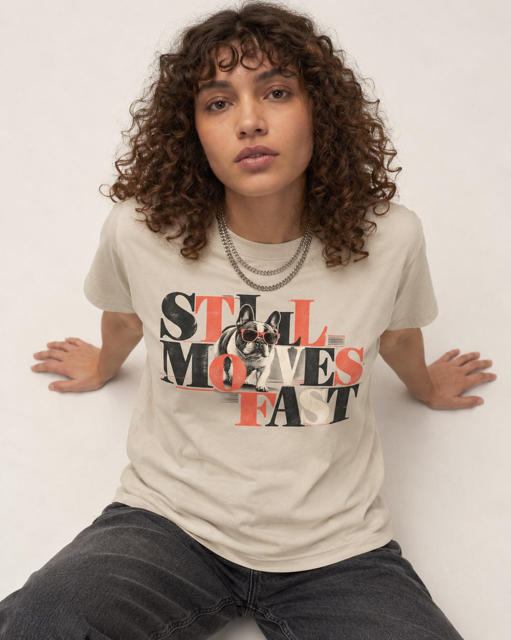 Frenchie Still Moves Fast T-Shirt in Sand, worn by a seated model