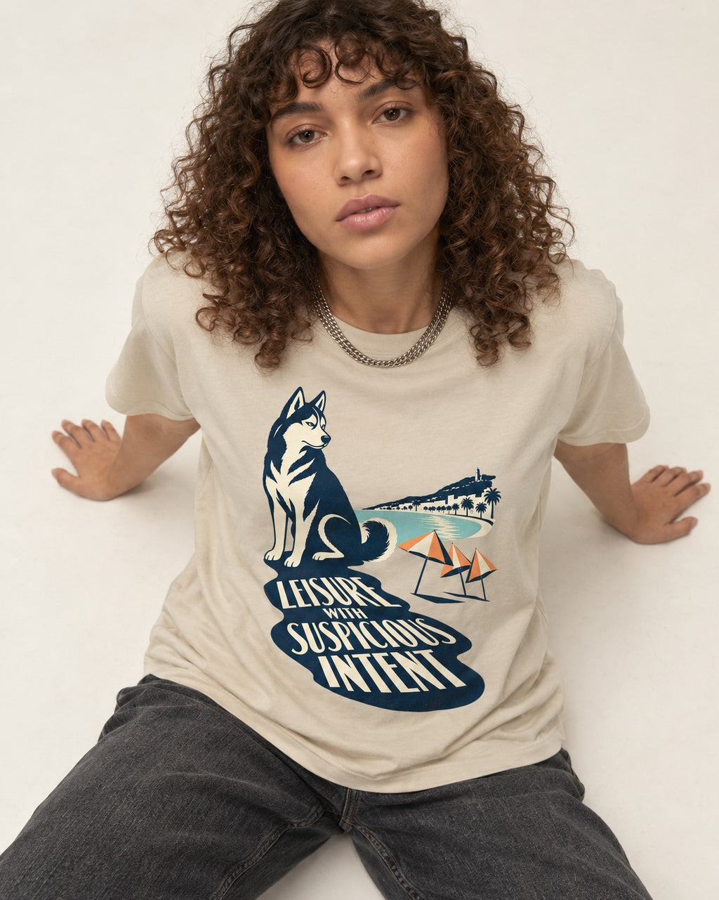 Husky Leisure with Suspicious Intent T-Shirt in Sand, worn by a seated model