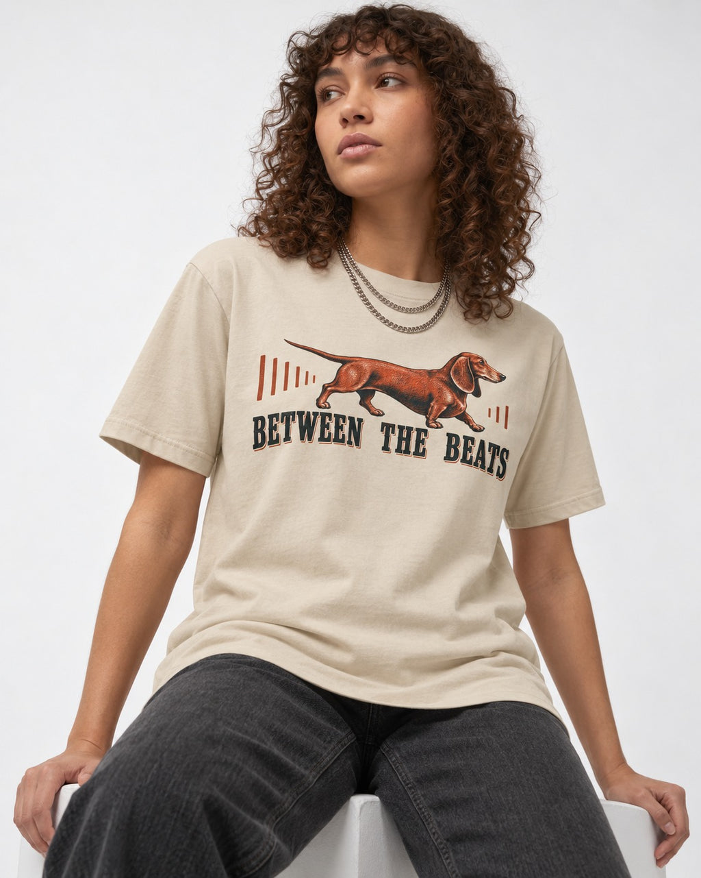 Dachshund Between the Beats T-Shirt in Sand, worn by a seated model