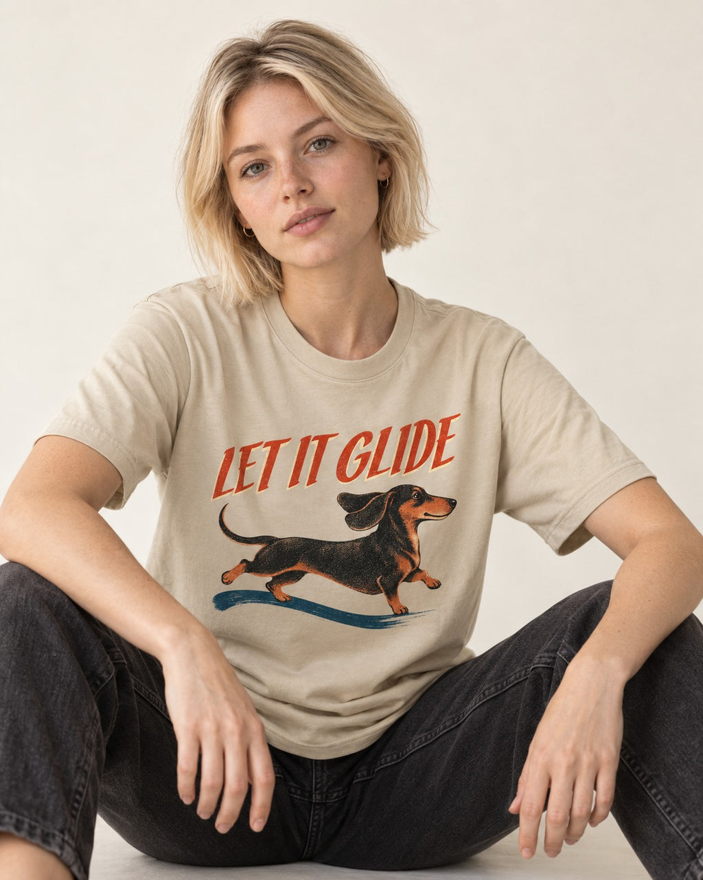 Let It Glide Dachshund T-Shirt in Sand, worn by a seated model