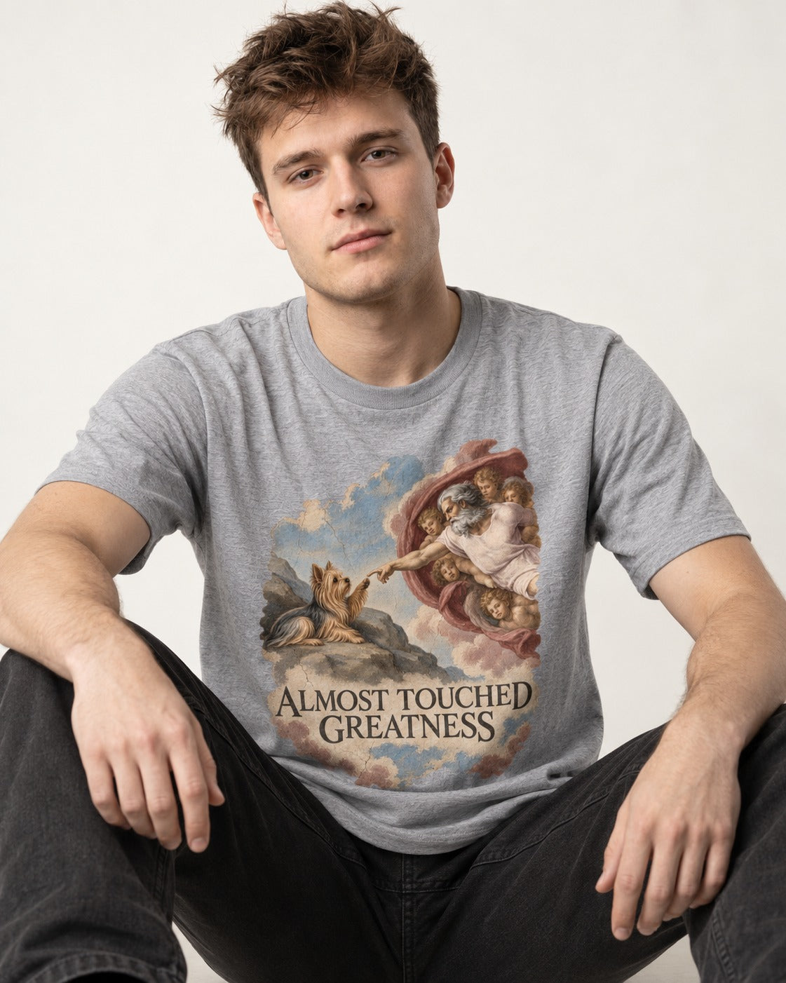Yorkshire Terrier Almost Touched Greatness Creation Parody Graphic T-Shirt in Sport Grey, worn by a seated model