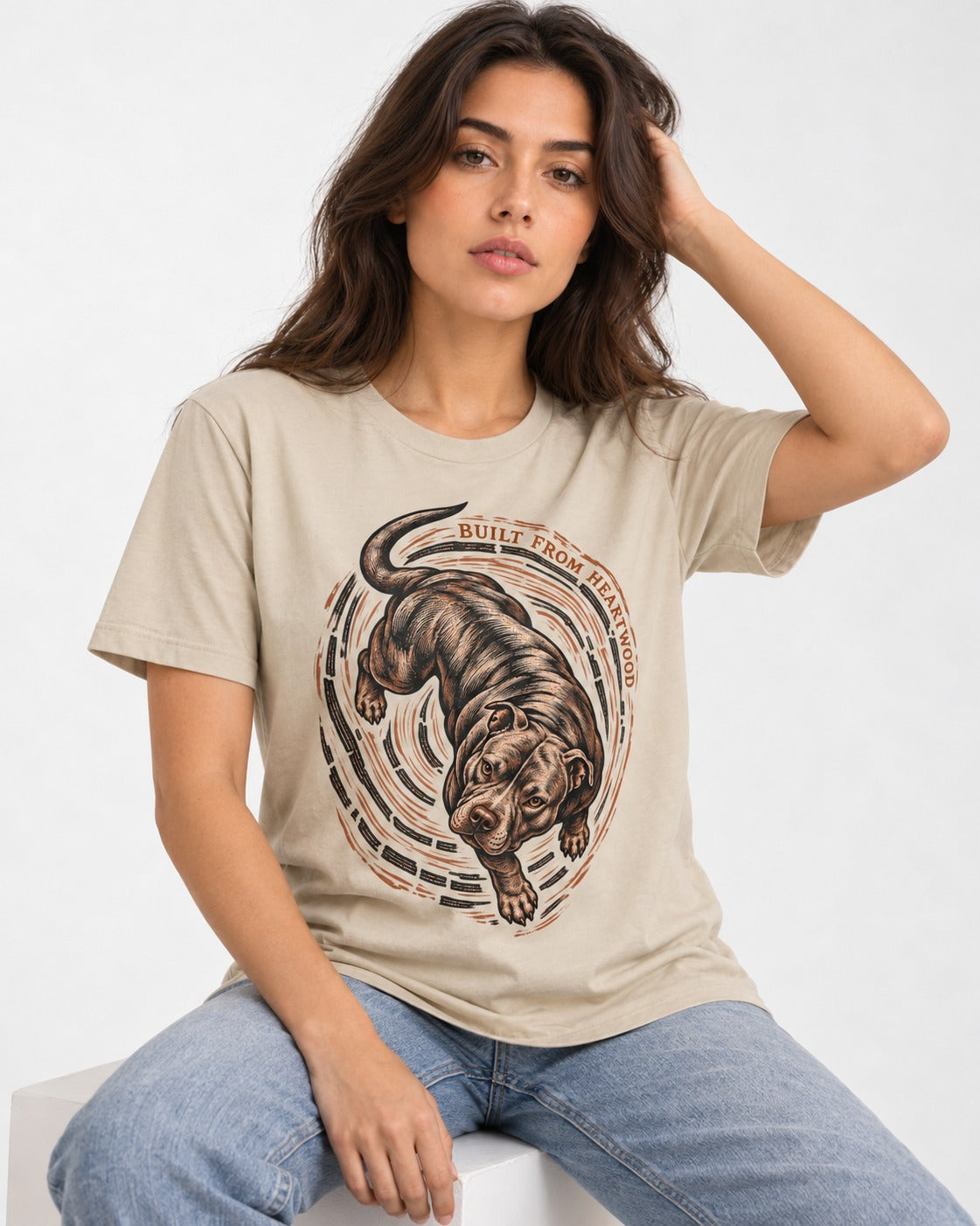 Pitbull Built From Heartwood T-Shirt in Sand, worn by a seated model