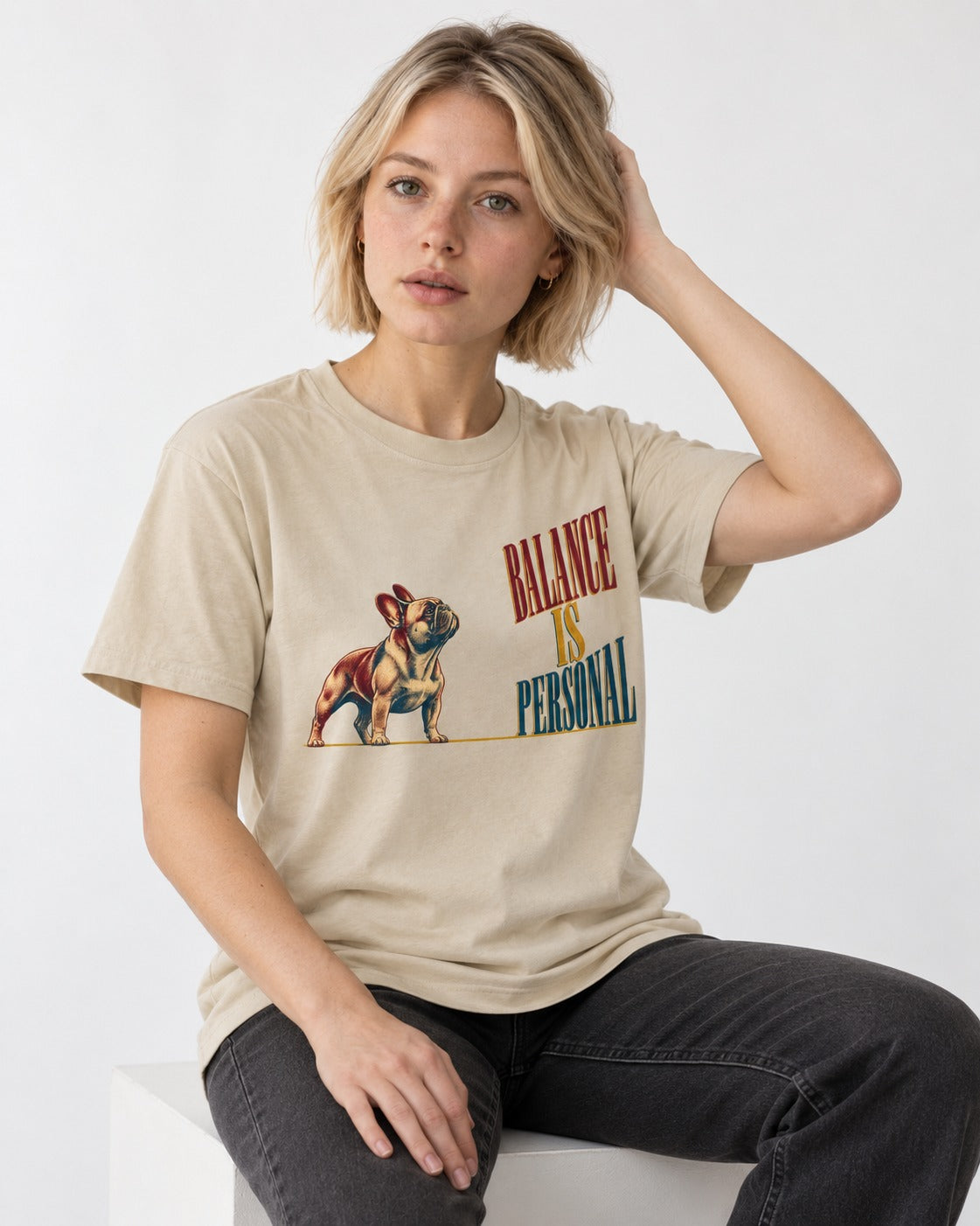 Frenchie Balance Is Personal T-Shirt in Sand, worn by a seated model