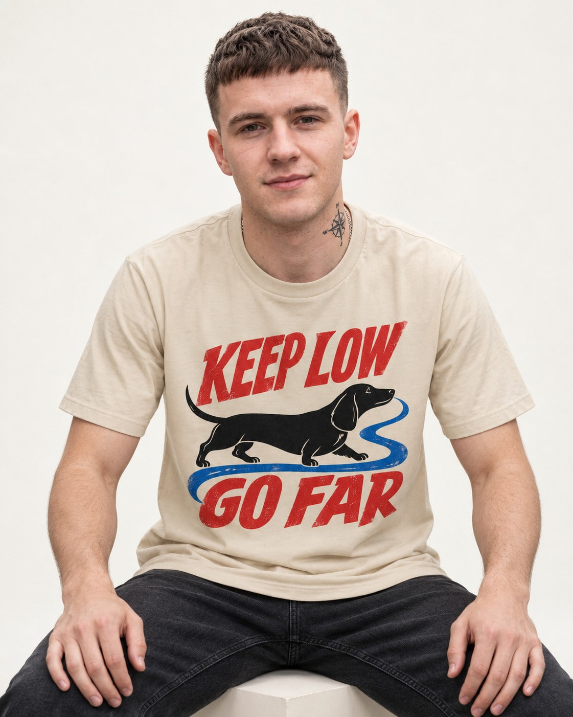 Keep Low Go Far Dachshund T-Shirt in Sand, worn by a seated model