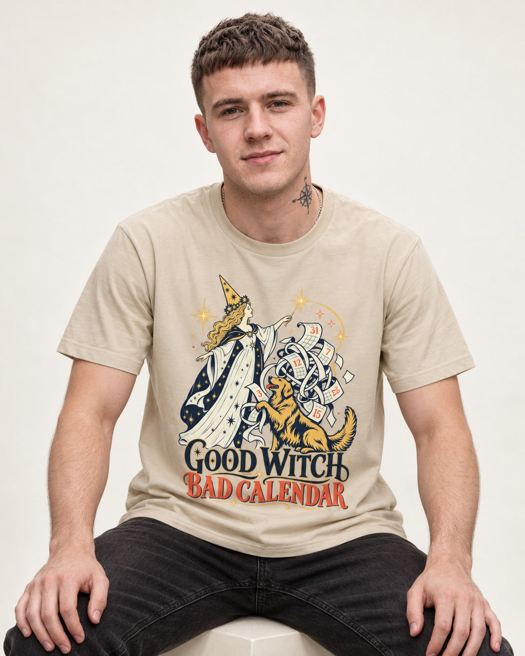Good Witch Bad Calendar Golden Retriever T-Shirt in Sand, worn by a seated model