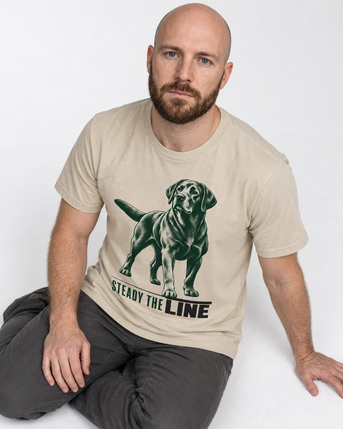 Steady the Line Labrador Retriever T-Shirt in Sand, worn by a seated model