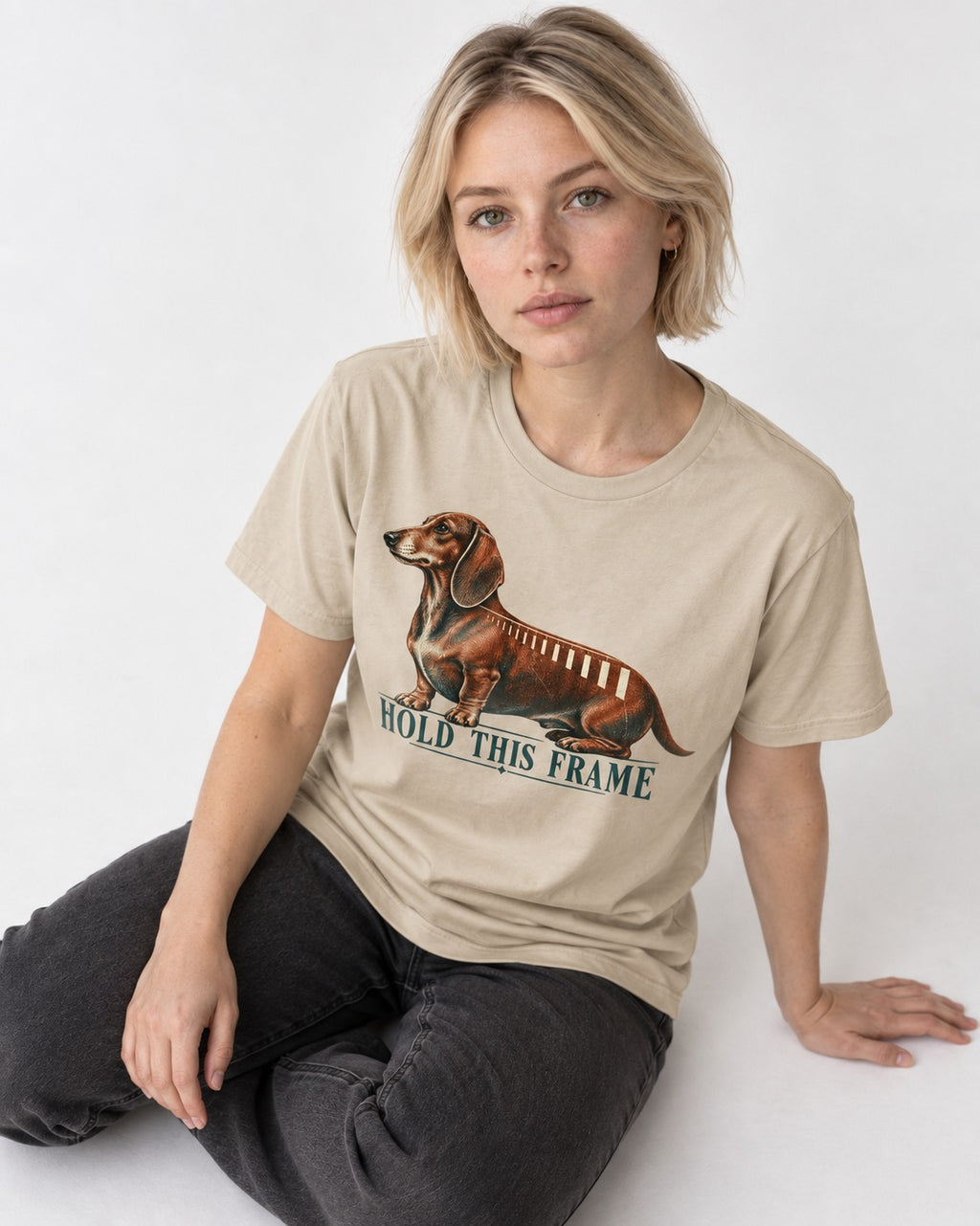 Dachshund Hold This Frame T-Shirt in Sand, worn by a seated model
