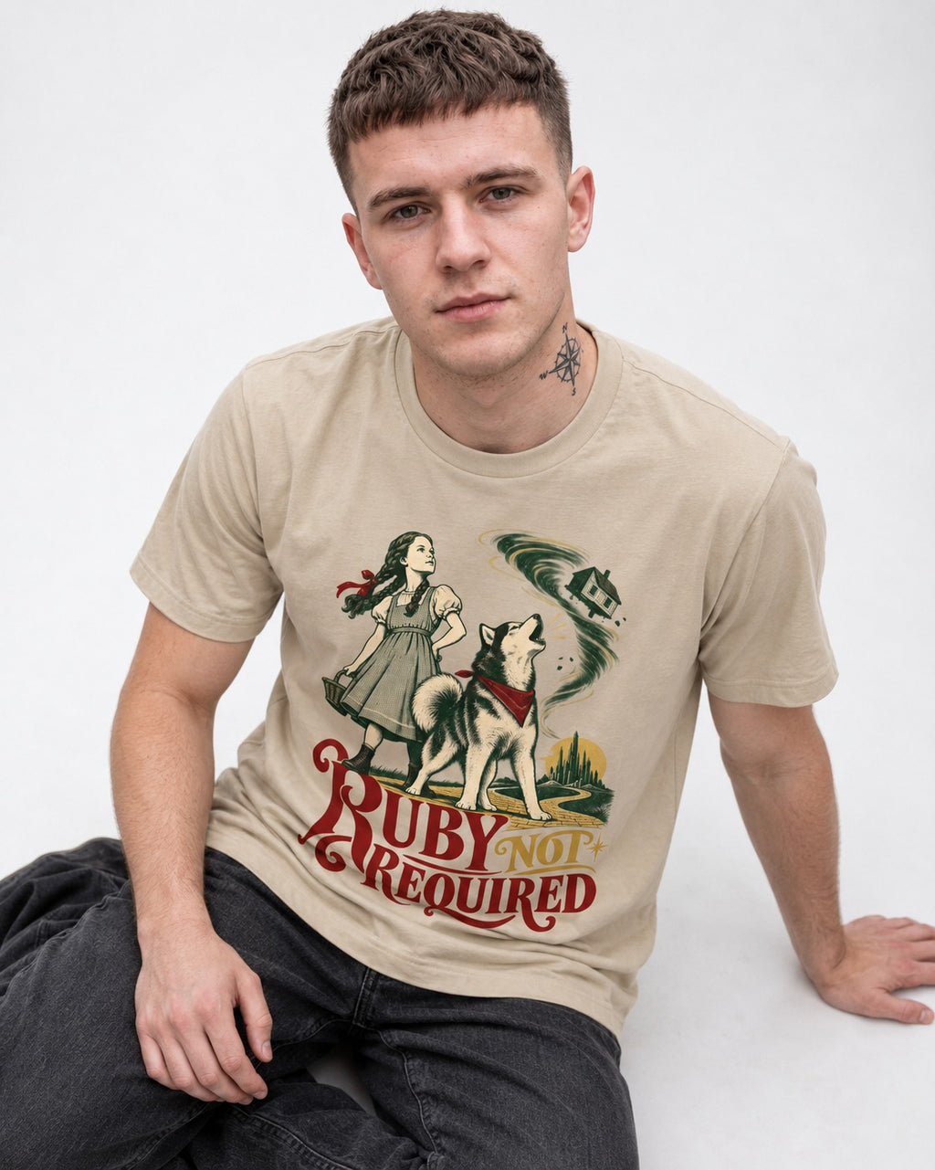 Ruby Not Required for Husky T-Shirt in Sand, worn by a seated model