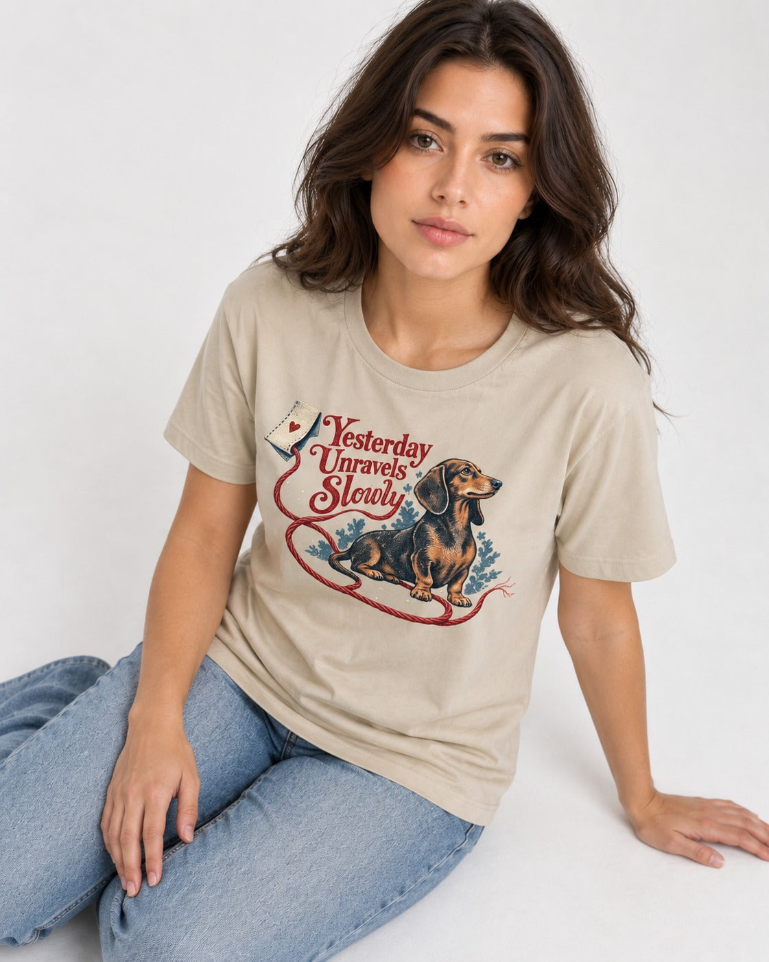 Yesterday Unravels Slowly with Dachshund T-Shirt in Sand, worn by a seated model