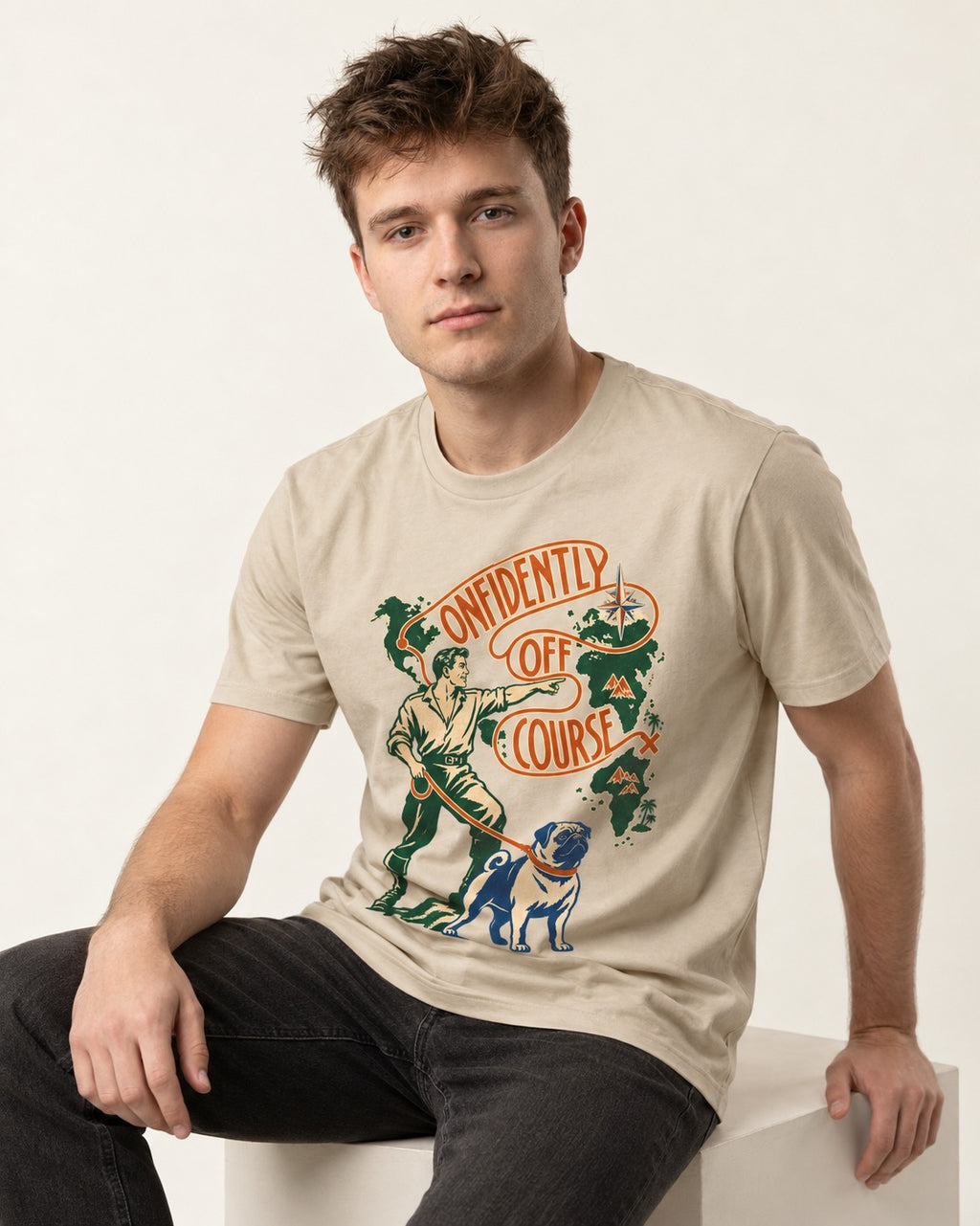 Pug Confidently Off Course T-Shirt in Sand, worn by a seated model