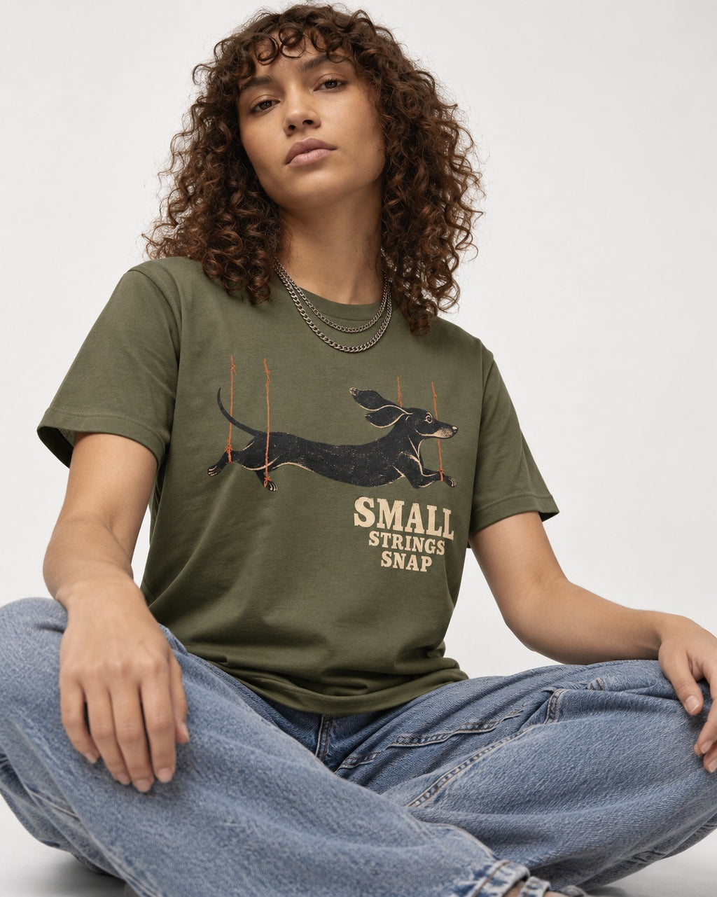 Dachshund Small Strings Snap Marionette Graphic T-Shirt in Heather Military Green, worn by a seated model