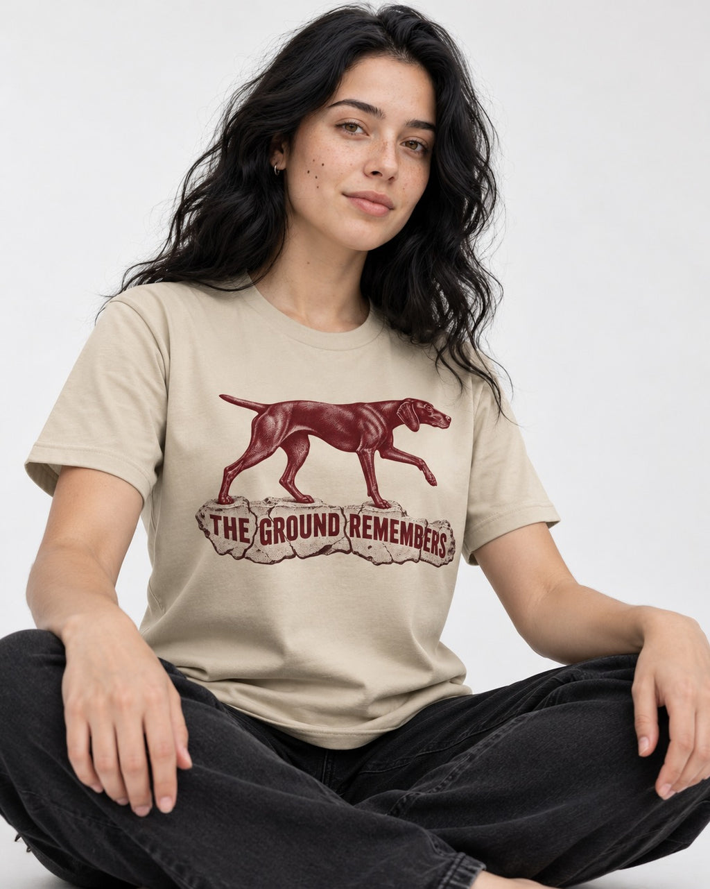 The Ground Remembers German Shorthaired Pointer T-Shirt in Sand, worn by a seated model