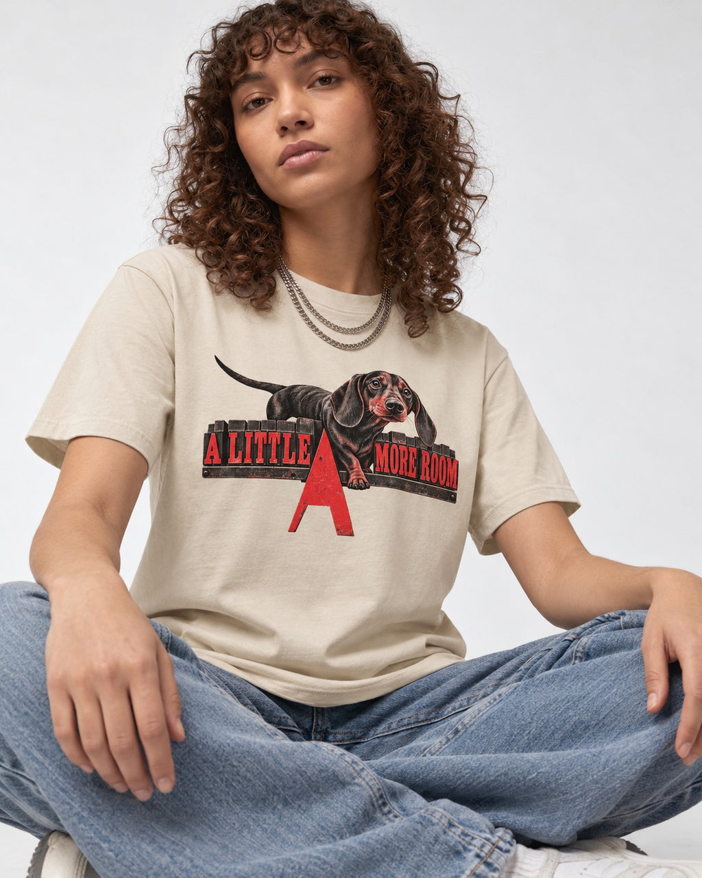 More Room for Dachshund T-Shirt in Sand, worn by a seated model