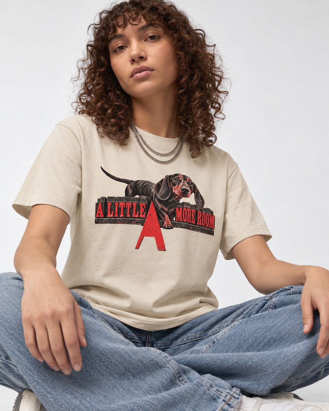 More Room for Dachshund T-Shirt in Sand, worn by a seated model