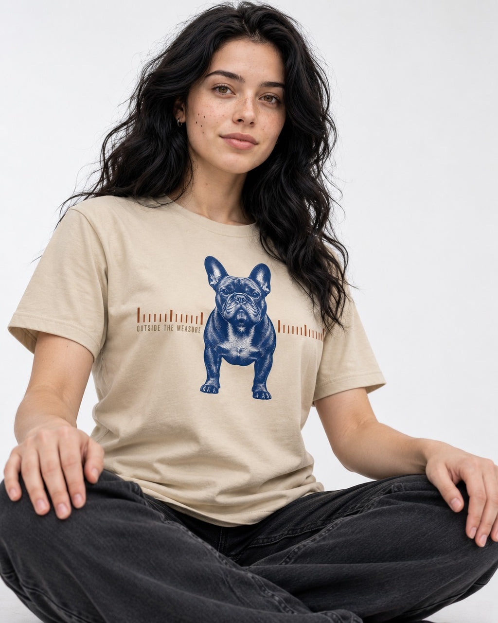 Frenchie Outside the Measure T-Shirt in Sand, worn by a seated model
