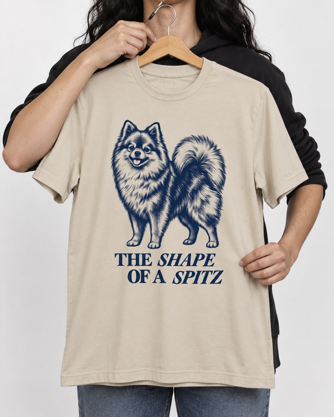 The Shape of a Pomeranian T-Shirt in Sand, held up on a hanger